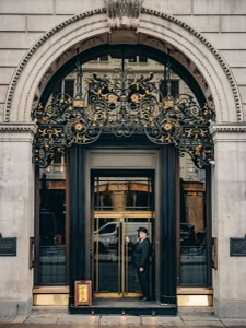 A doorman at the wrought-iron entrance of a grand Piccadilly dining room